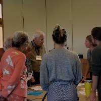 Older and younger people stand around a table